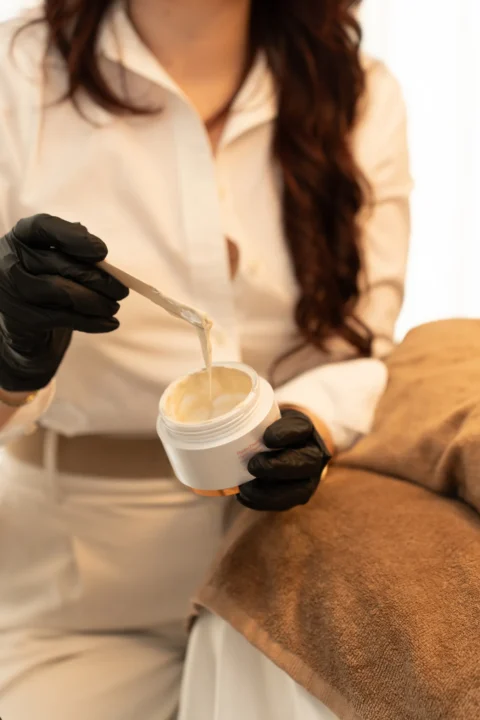 Marin neemt met een spatel verzorgende creme uit een potje voor een gelaatsbehandeling