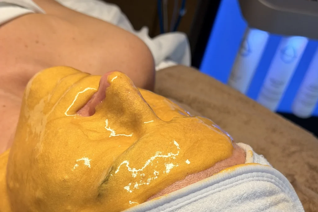 Klant met een oranje gelmasker en een witte KRX Aesthetics-haarband tijdens een gelaatsbehandeling